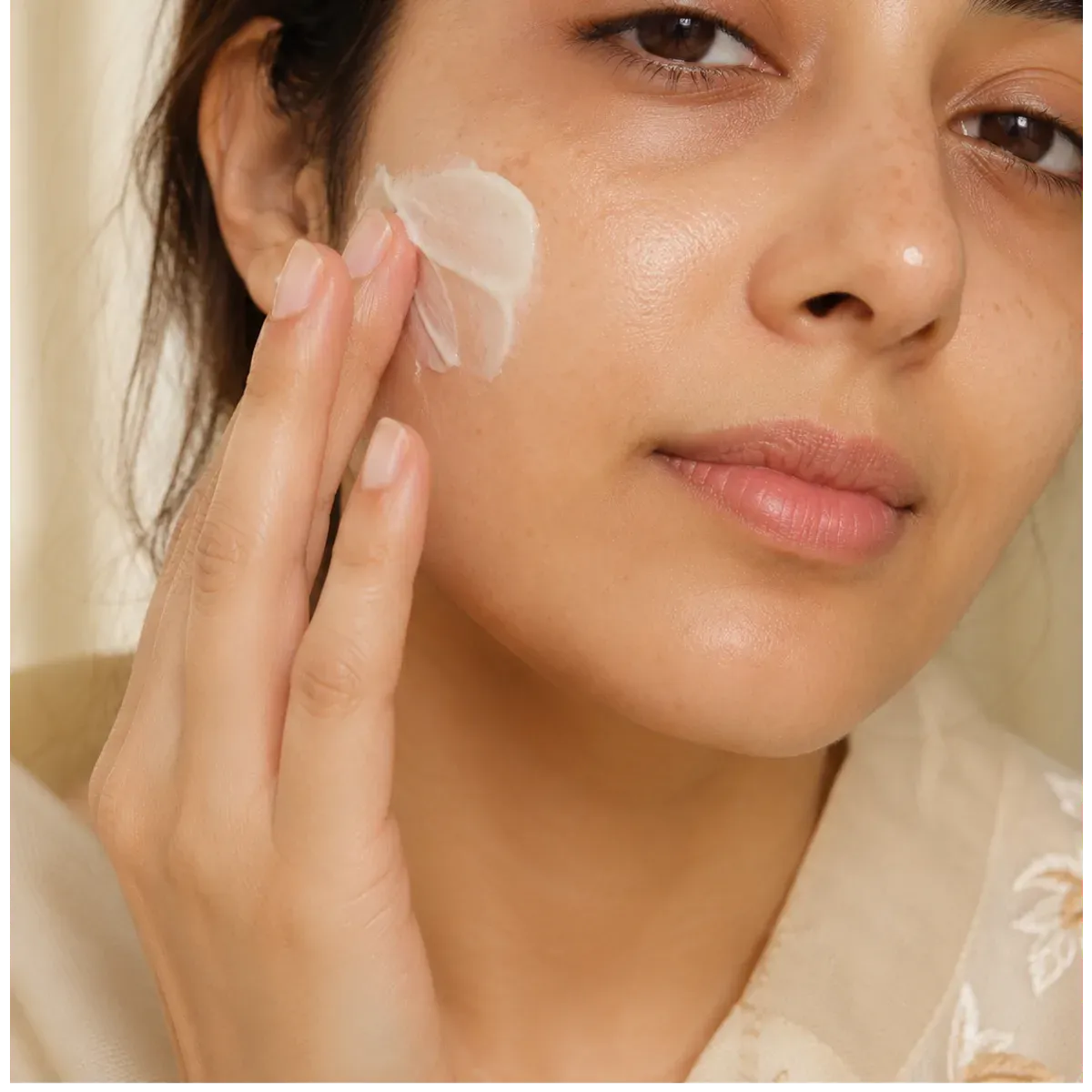 A woman applying TJs cream to her cheek in natural daylight